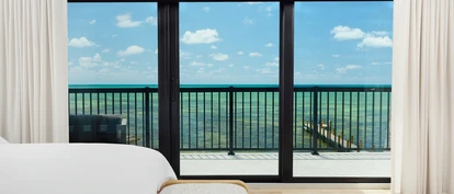 PGT SGD770 sliding glass door framing an oceanfront balcony view from a bright coastal bedroom