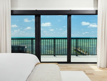 PGT SGD770 sliding glass door framing an oceanfront balcony view from a bright coastal bedroom