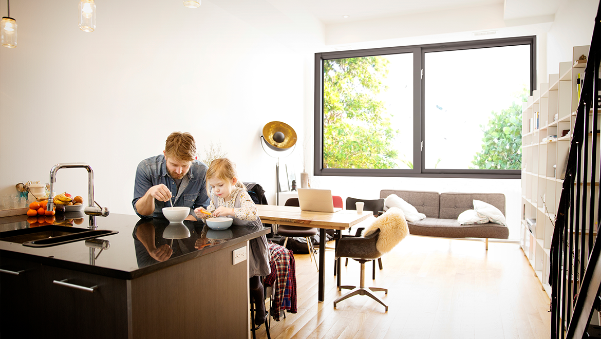 Man and daughter enjoying breakfast in room with impact resistant, noise reducing windows