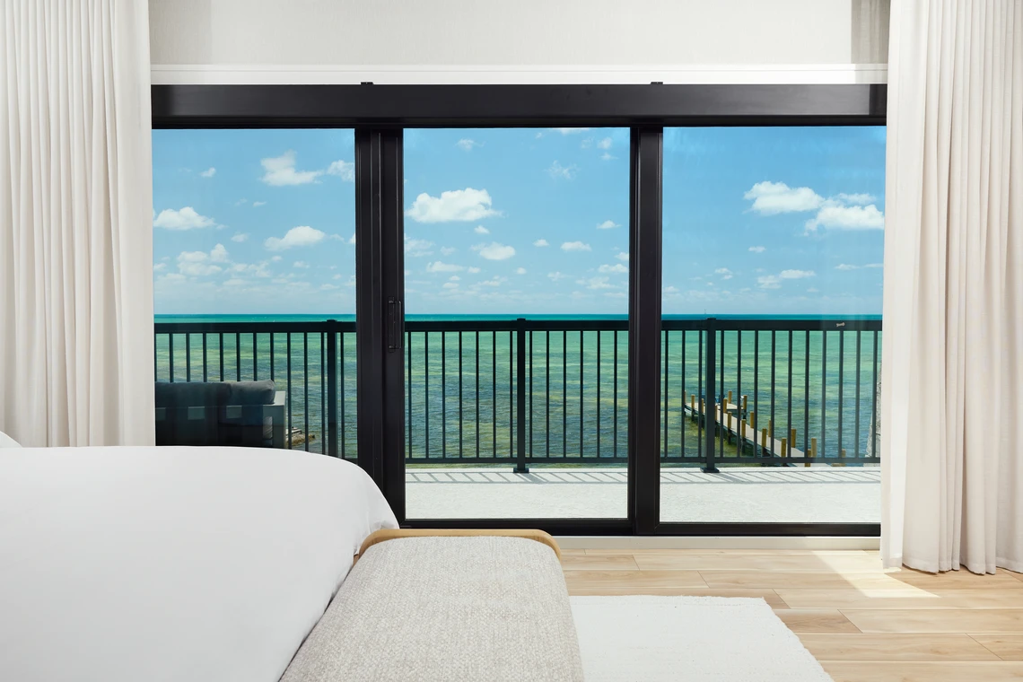 PGT SGD770 sliding glass door framing an oceanfront balcony view from a bright coastal bedroom