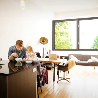 Man and daughter enjoying breakfast in room with impact resistant, noise reducing windows