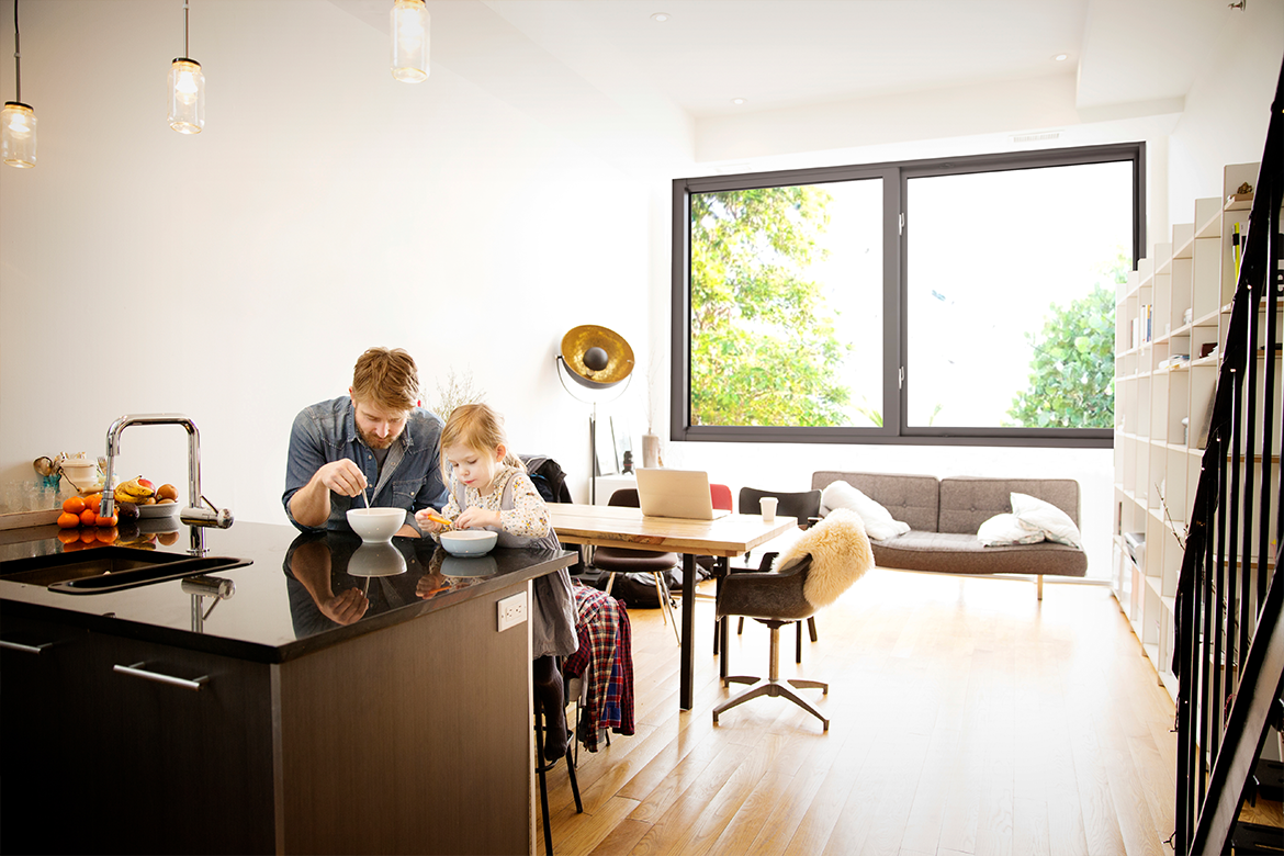 Man and daughter enjoying breakfast in room with impact resistant, noise reducing windows
