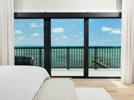 PGT SGD770 sliding glass door framing an oceanfront balcony view from a bright coastal bedroom