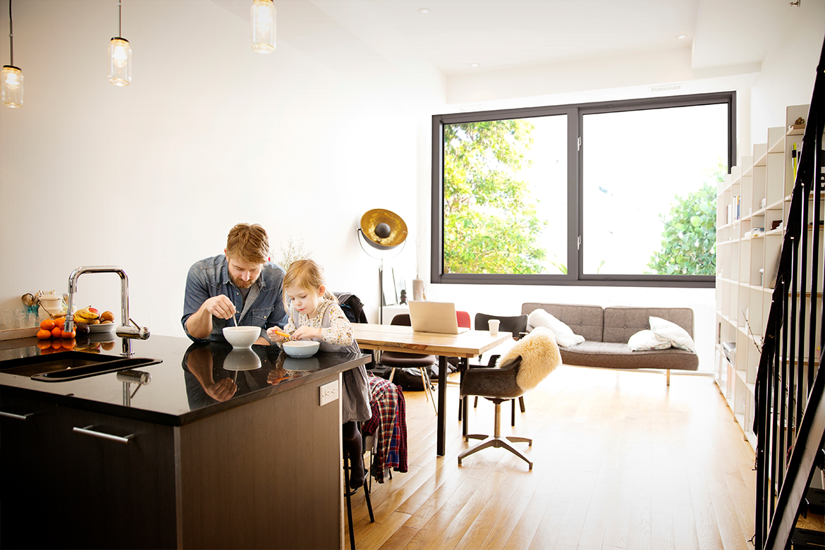 Man and daughter enjoying breakfast in room with impact-resistant, noise reducing windows
